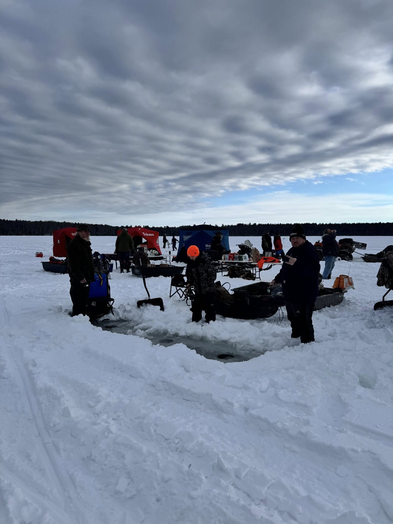 Wide view of the ice fishing setup with dramatic winter sky